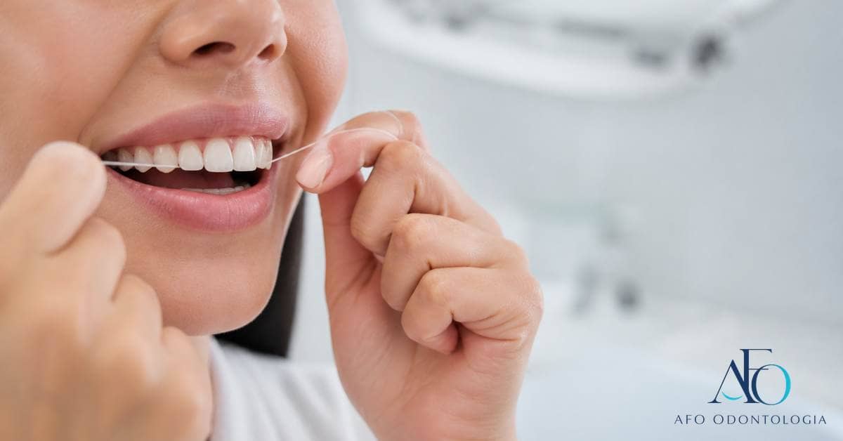 Mão usando fio dental suavemente junto à gengiva em demonstração educativa